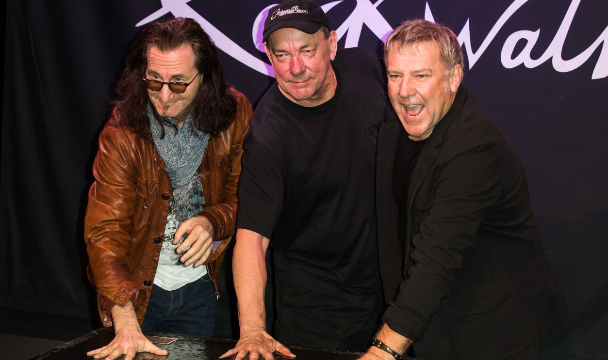 Gettyimages - 156771098, Rock Band Rush Gets Inducted Into Guitar Center's Historic RockWalk HOLLYWOOD, CA - NOVEMBER 20: (L-R) Musicians Geddy Lee, Neil Peart and Alex Lifeson of Rush are inducted into Guitar Center's historic RockWalk at Guitar Center on November 20, 2012 in Hollywood, California.