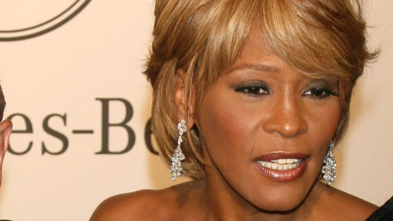 Clive Davis in black suit and Whitney Houston in black dress looking nd smiling at camera - 2006