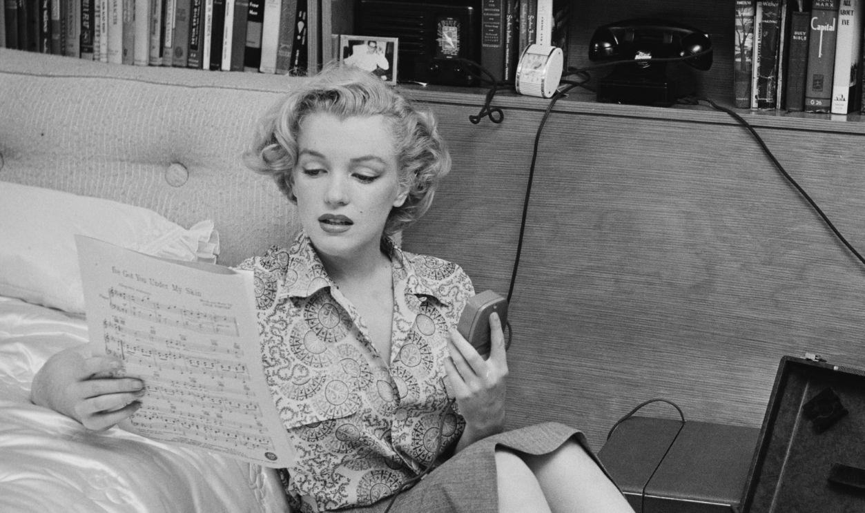 American actress Marilyn Monroe (1926 - 1962) reading sheet music while sitting on a bedroom floor with a tape player on the side, US, circa 1950.