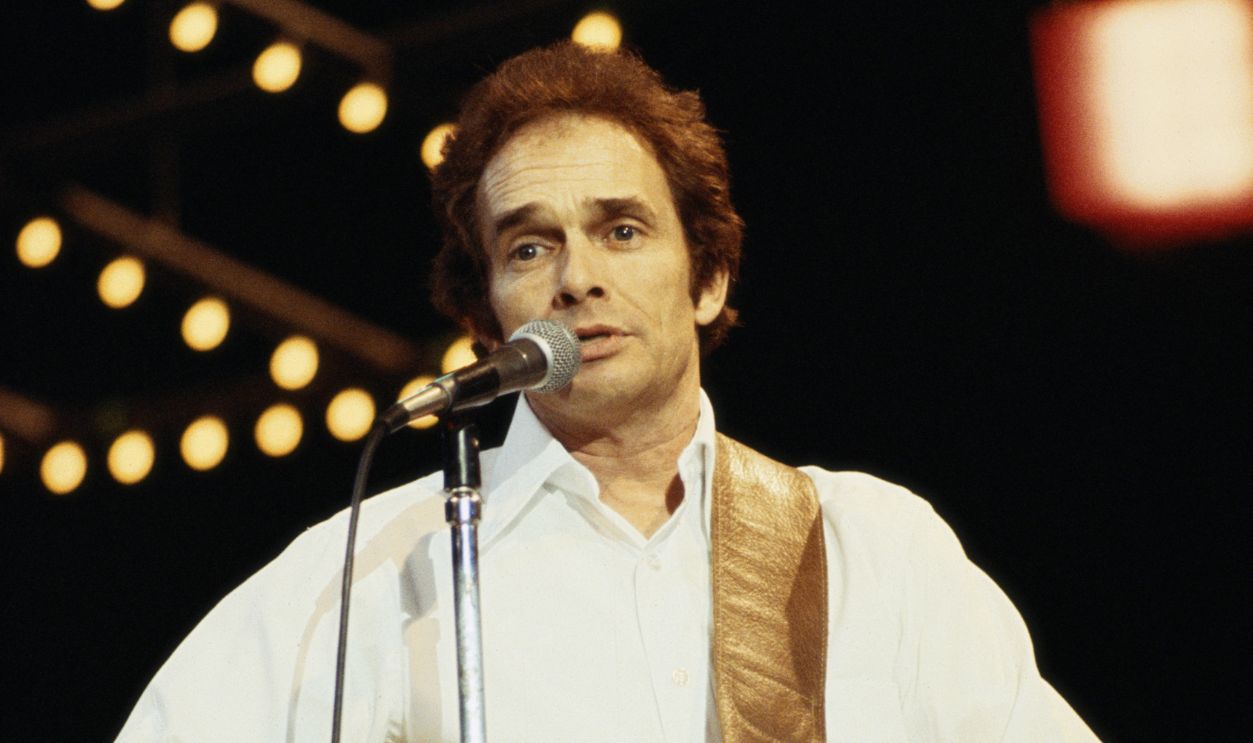 Merle Haggard, U.S. country singer, playing the guitar while singing into a microphone in concert, circa 1975.