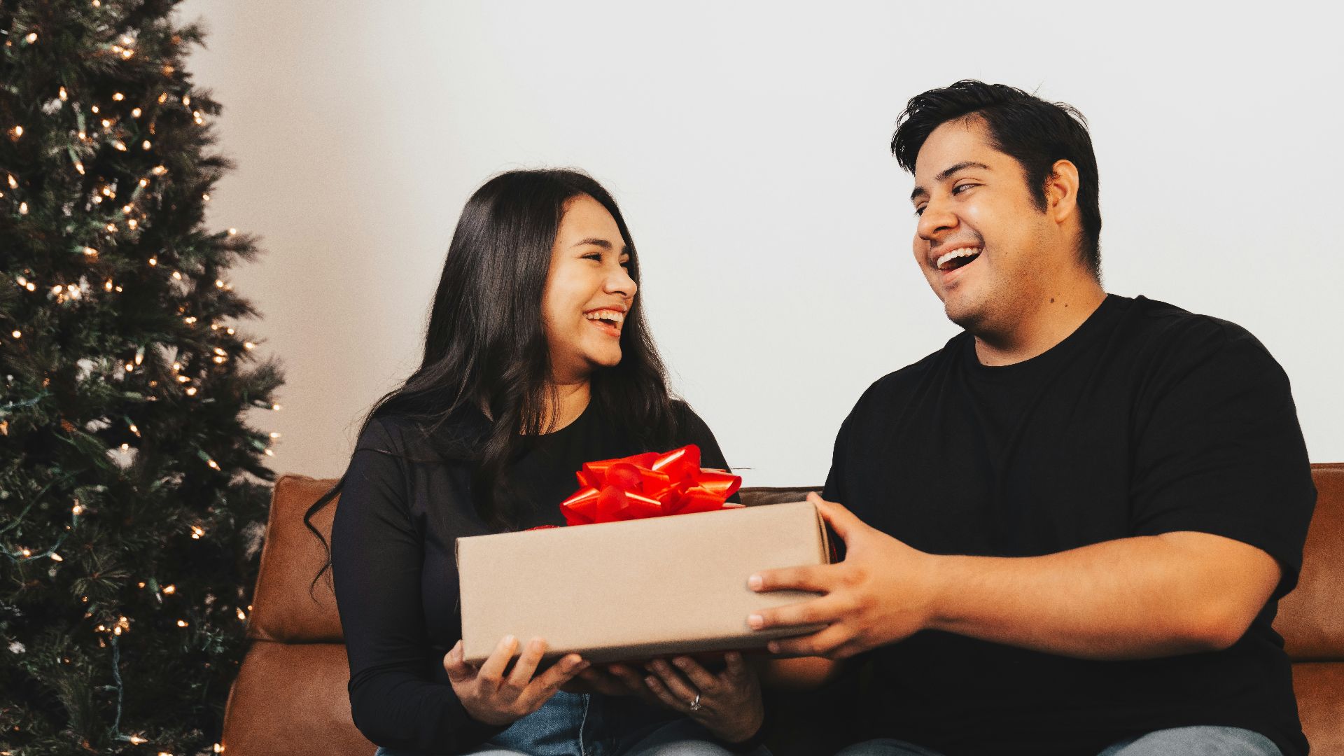 A man and woman sitting on a couch holding a box