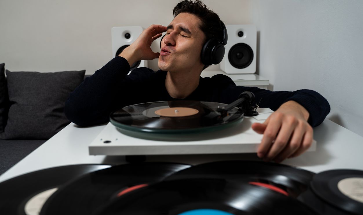 Emotional music lover is listening a vinyl record on a turntable player. Cheerful hipster is listening to music by vintage vinyl records and feeling real emotions of music lover.