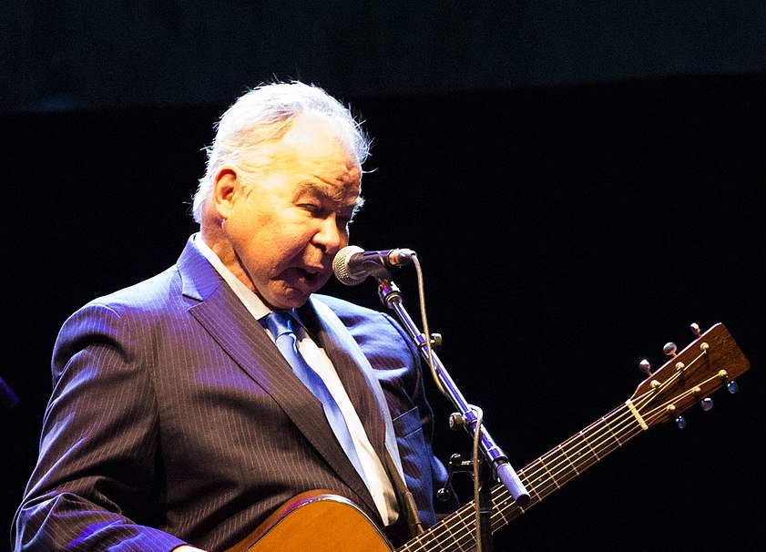 John Prine in a suit performing on stage