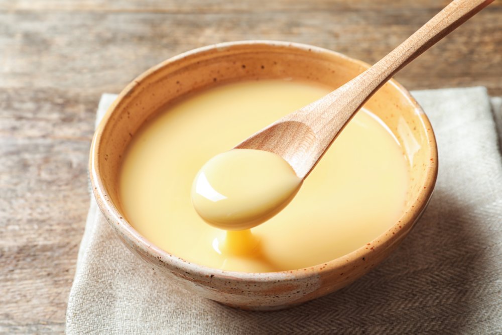 Close Up Photo of Spoon with pouring condensed milk over bowl on table