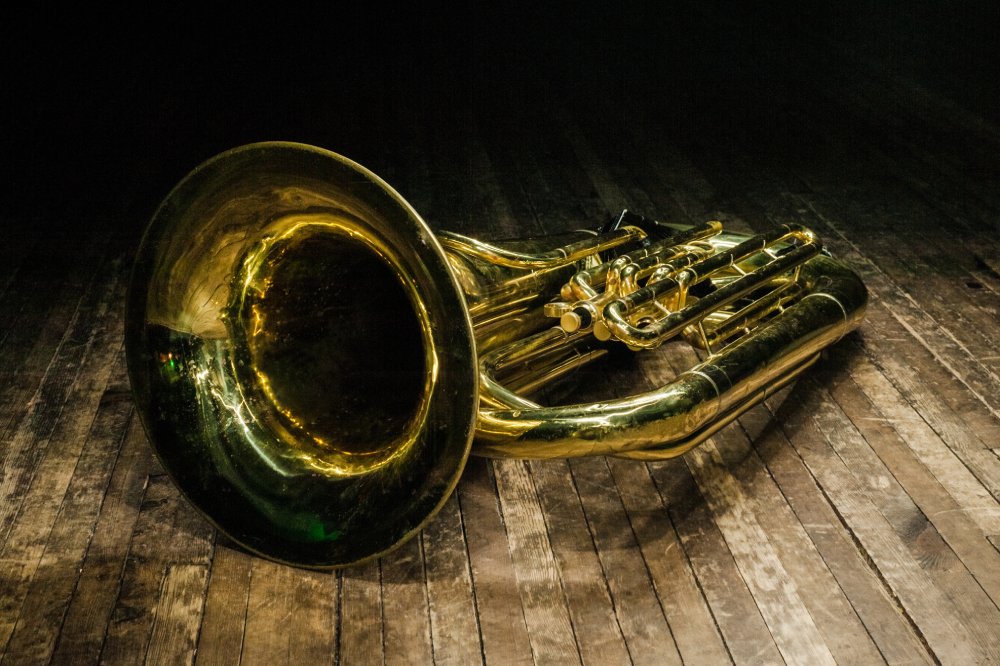 Close Up Photo of golden brass instrument tuba lies on a brown wooden stage