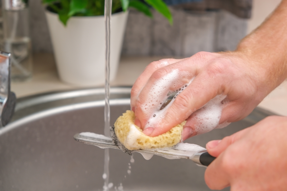 A man washes a sharp steel dirty kitchen knife