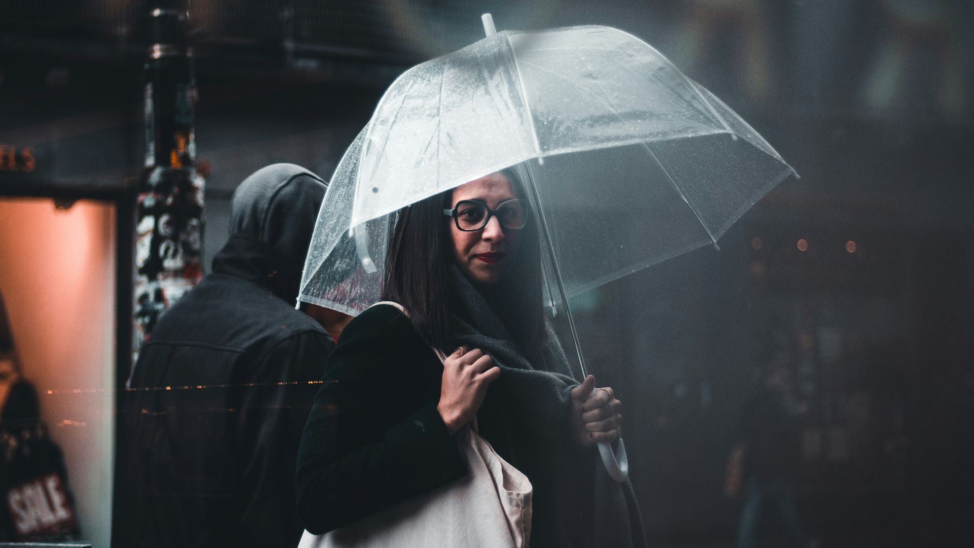 selective focus photography of woman carrying white bag while holding clear umbrella near person wearing hoodie outdoor