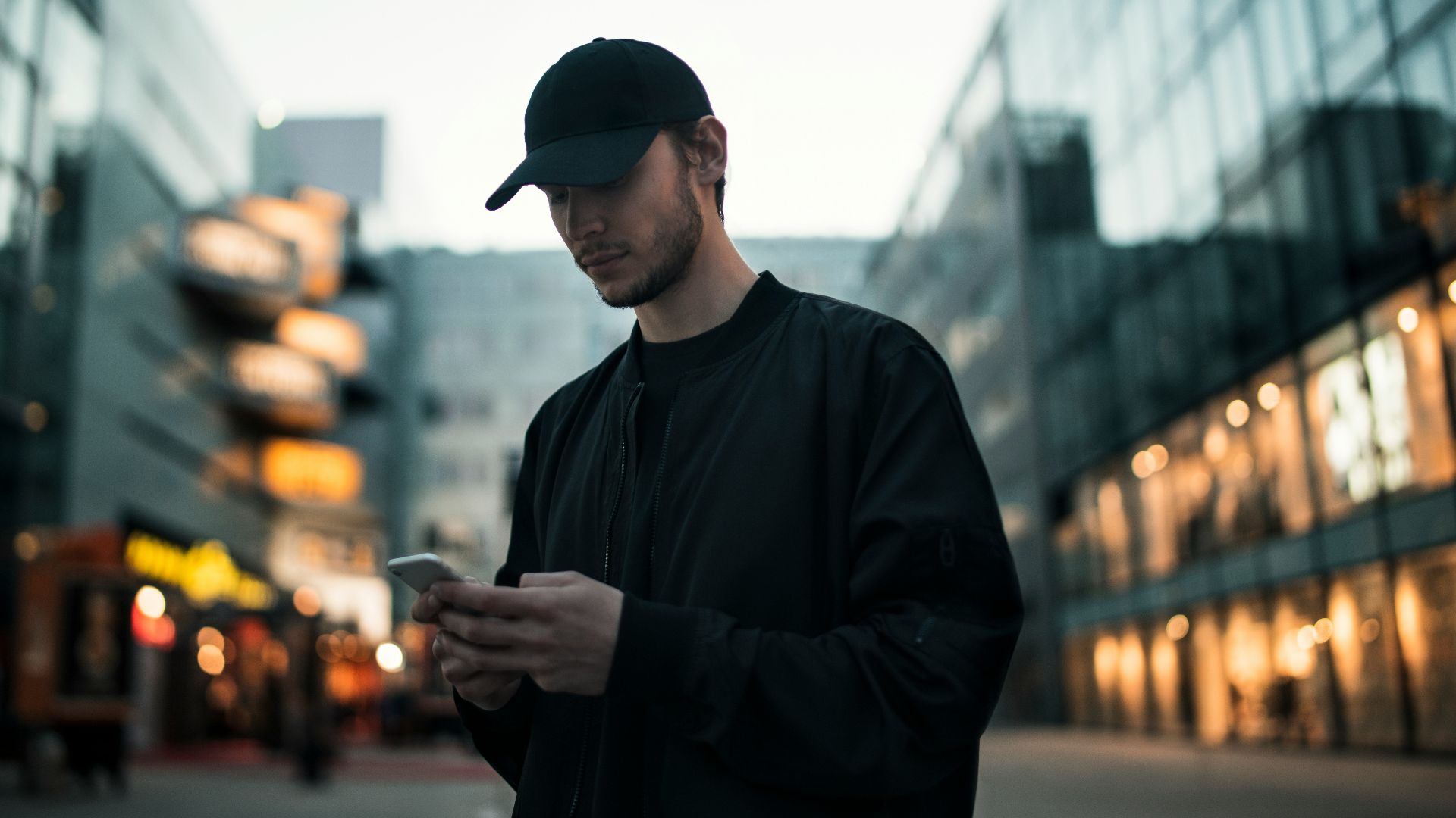man in black jacket wearing black fitted cap while using phone