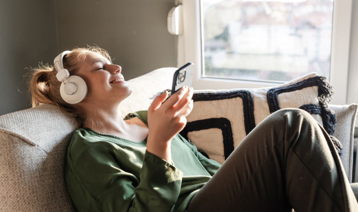 Young woman relaxing on a sofa and listening music on her phone via headphones