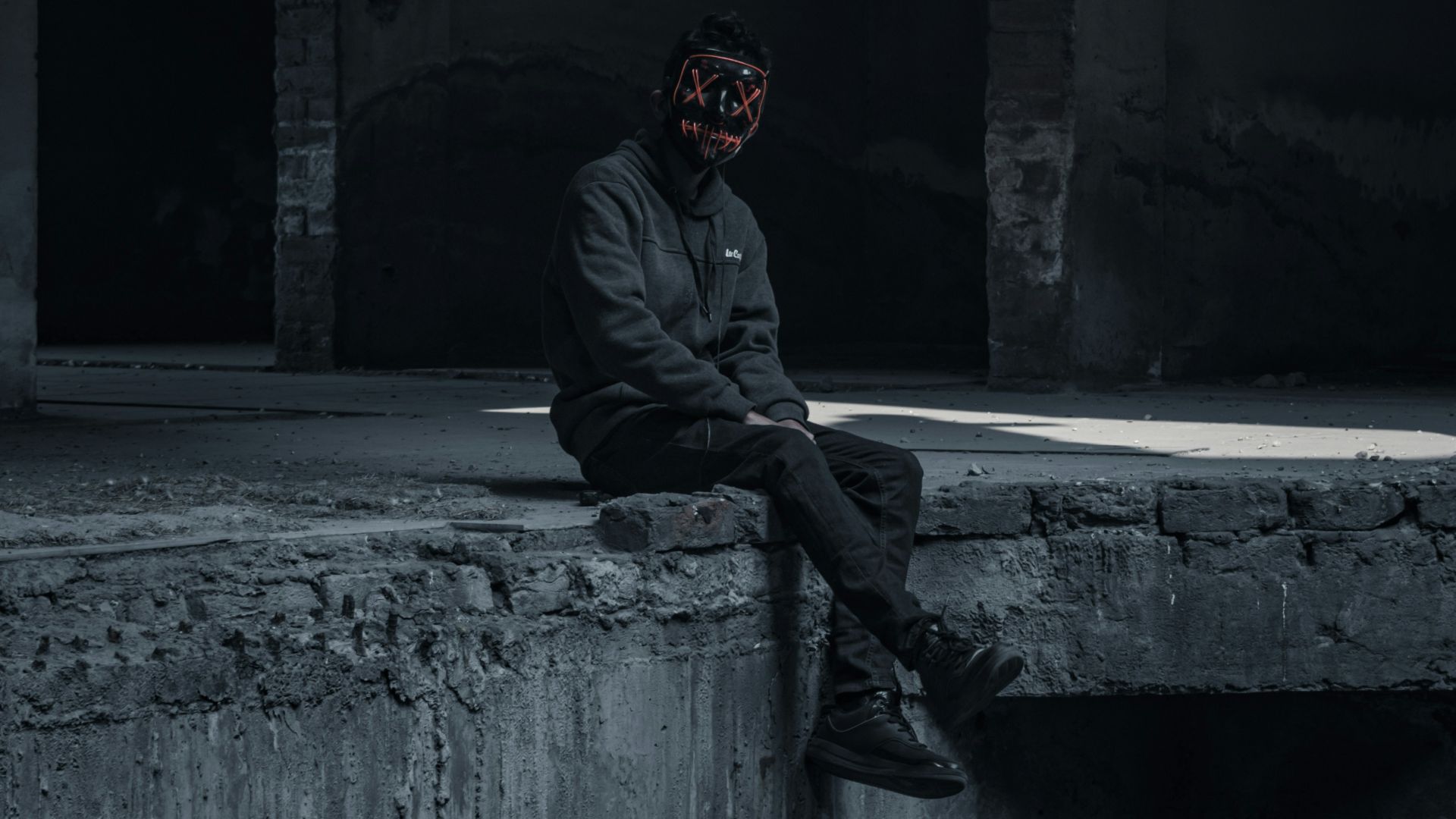 man in black hoodie and black pants sitting on gray concrete floor