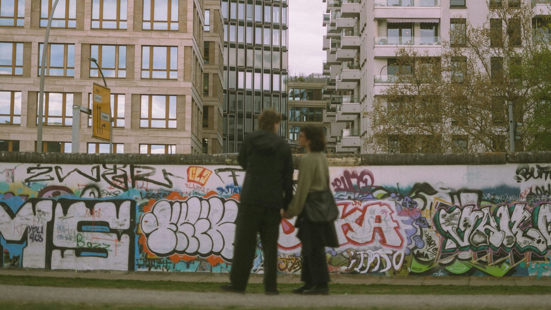 People stand before a graffiti wall and city buildings.