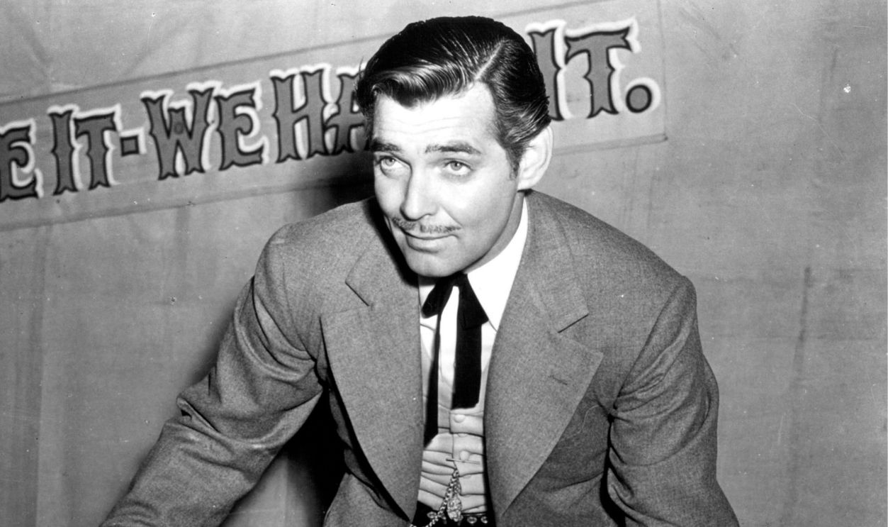 American actor Clark Gable (1901 - 1960) as con man Candy Johnson in the western 'Honky Tonk', 1941. A sign behind him reads 'Name it - We Have it'.