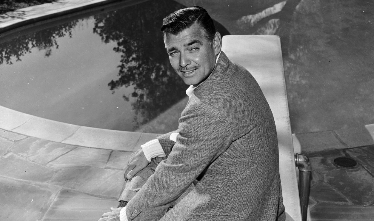  American leading man Clark Gable (1901 - 1960) sitting by the swimming pool at his home.