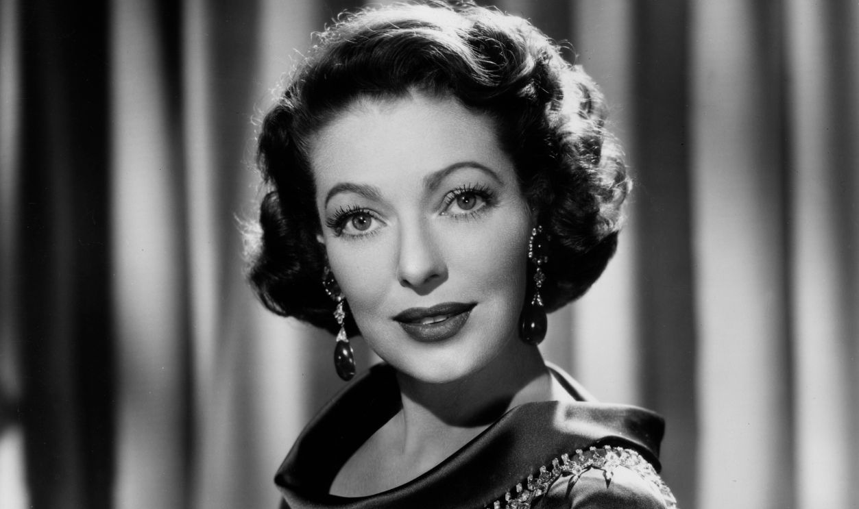 American actor Loretta Young (1913 - 2000) smiles in a satin dress, possibly in a promotional portrait for the television series, 'The Loretta Young Show'.