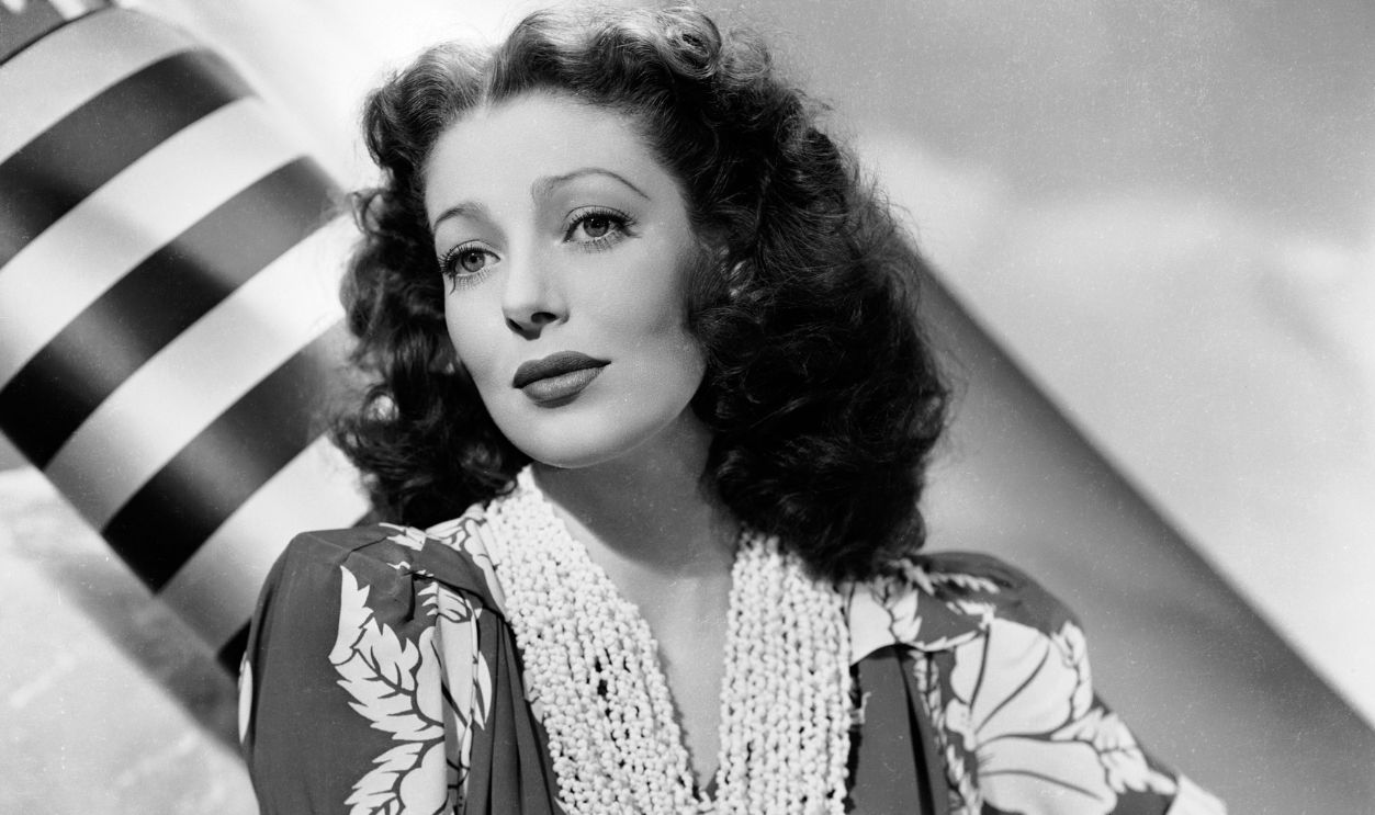 American actress Loretta Young (1913 - 2000) wearing a short-sleeved dress with a bold floral pattern and several necklaces.