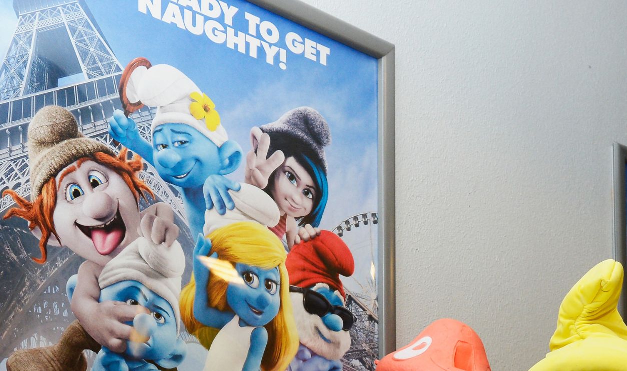 A dressed as a Smurf character poses by a poster of the movie 