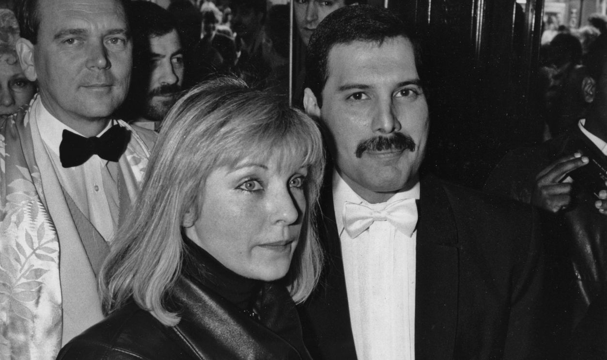 Singer Freddie Mercury (1946 - 1991) of British rock band Queen with his friend Mary Austin at an after-party in London for 'Dave Clark's Time - The Musical', 9th April 1986. Behind them is Queen's manager Jim Beach, .