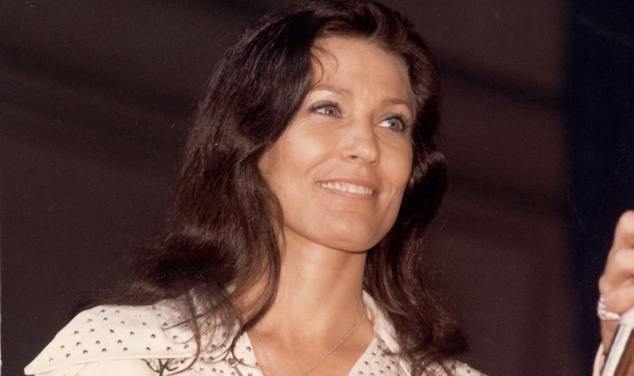 Loretta Lynn Smiles American country music singer and guitarist Loretta Lynn smiles as she looks at an unidentified person off-camera who holds a microphone, late 1970s.