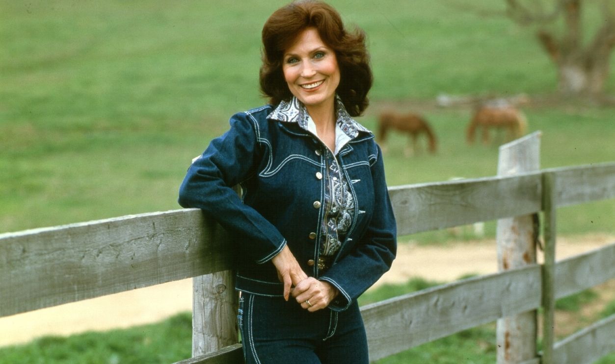 Loretta Lynn Full Length CIRCA 1972: Loretta Lynn poses for a portrait wearing a blue denim suit with cows in the background leaning up against a fence in circa 1972. 