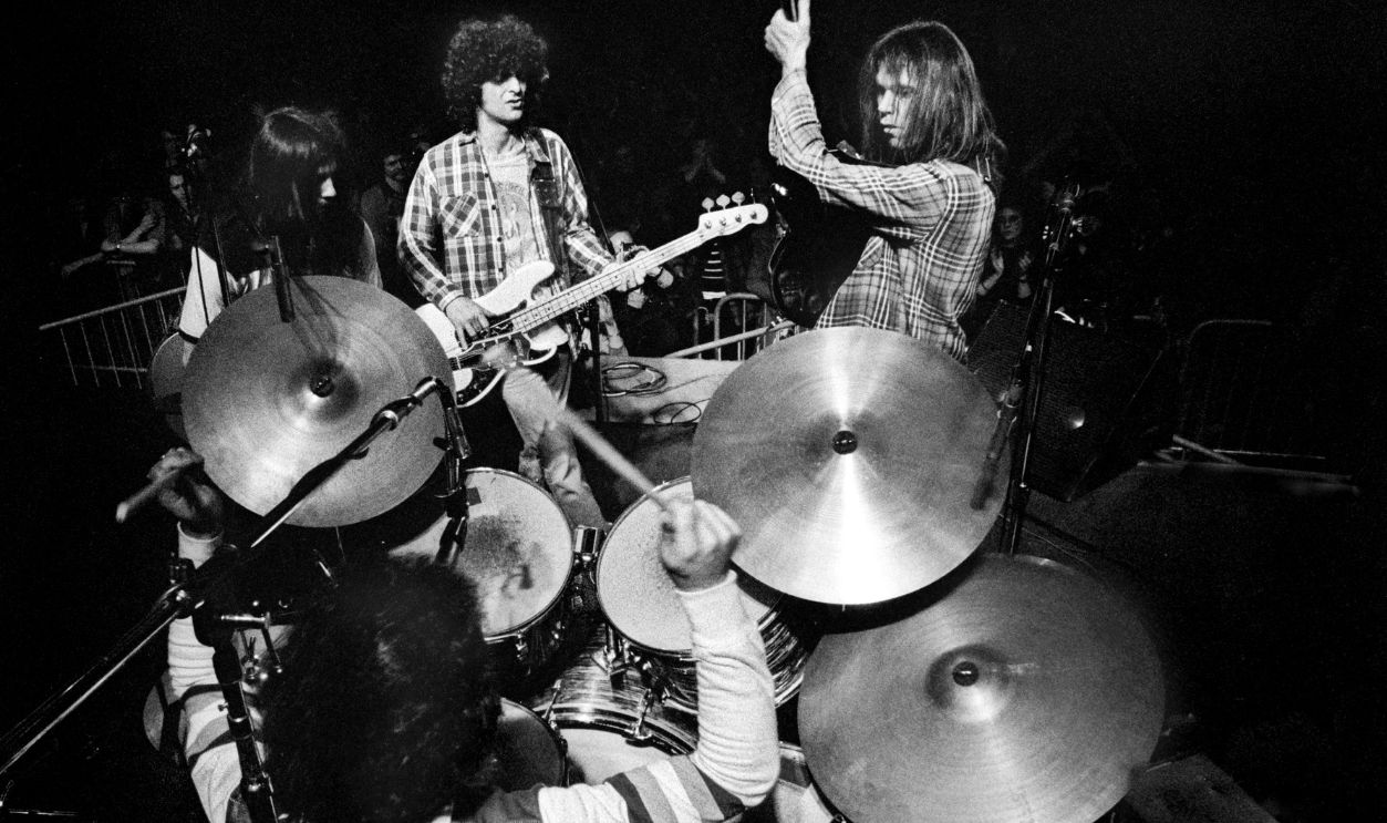 View from above and behind the drums at the back of the stage as Neil Young & Crazy Horse perform on stage during their 1976 tour of Europe, Ahoy Hallen, Rotterdam, Netherlands, 24th March 1976. L-R Frank Sampedro, Ralph Molina, Billy Talbot, Neil Young. 