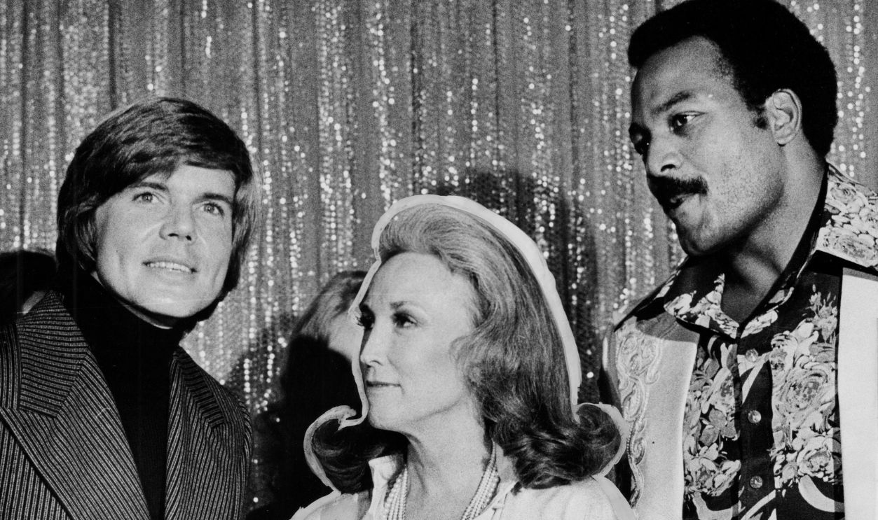 Actor John Davidson (left), and former football star Jim Brown (right) appear with Cosmopolitan Magazine's editor Helen Gurley Brown (center) at the Blue Angel nightclub in Manhattan on January 21, 1974