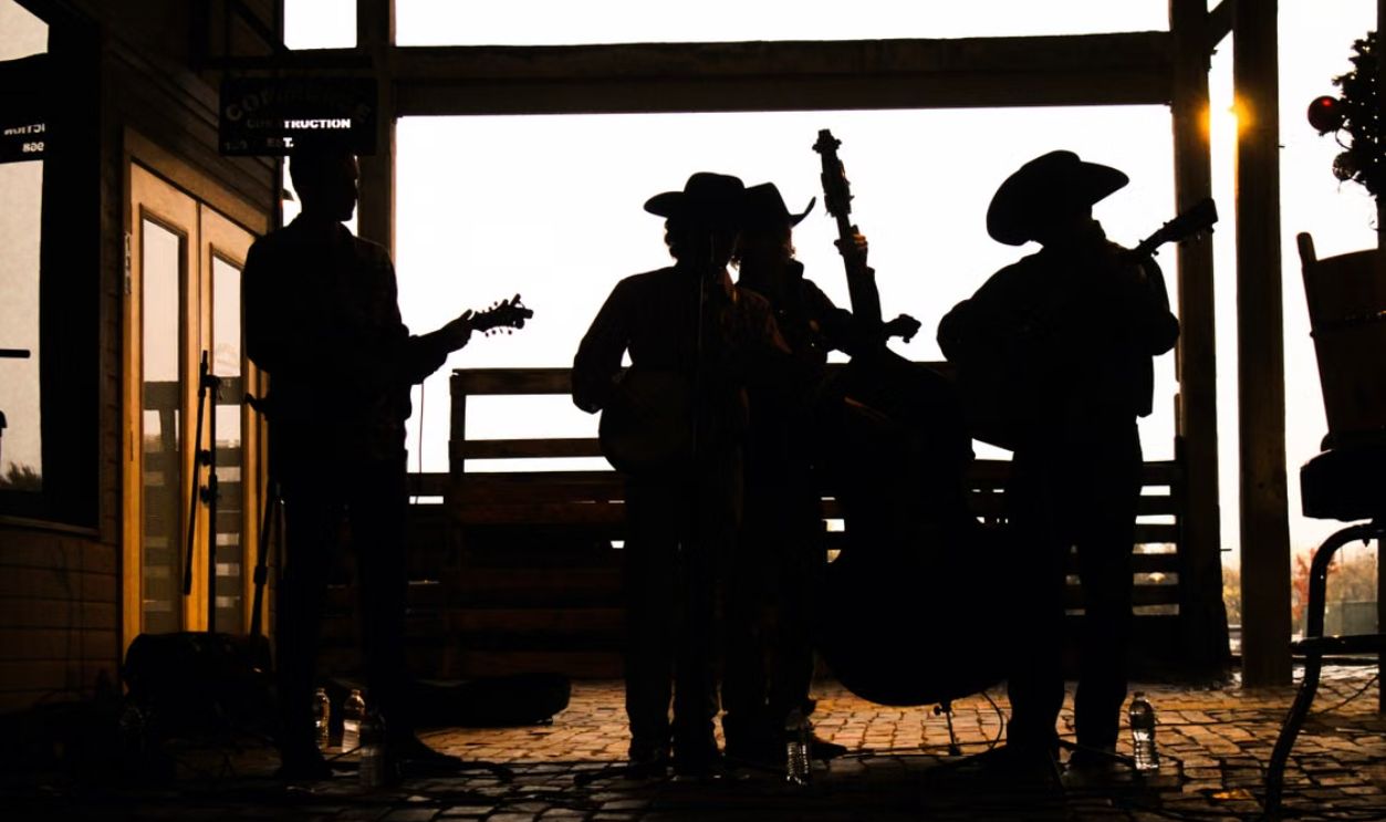 Silhouette of musicians playing string instruments outdoors, creating a rustic and artistic vibe