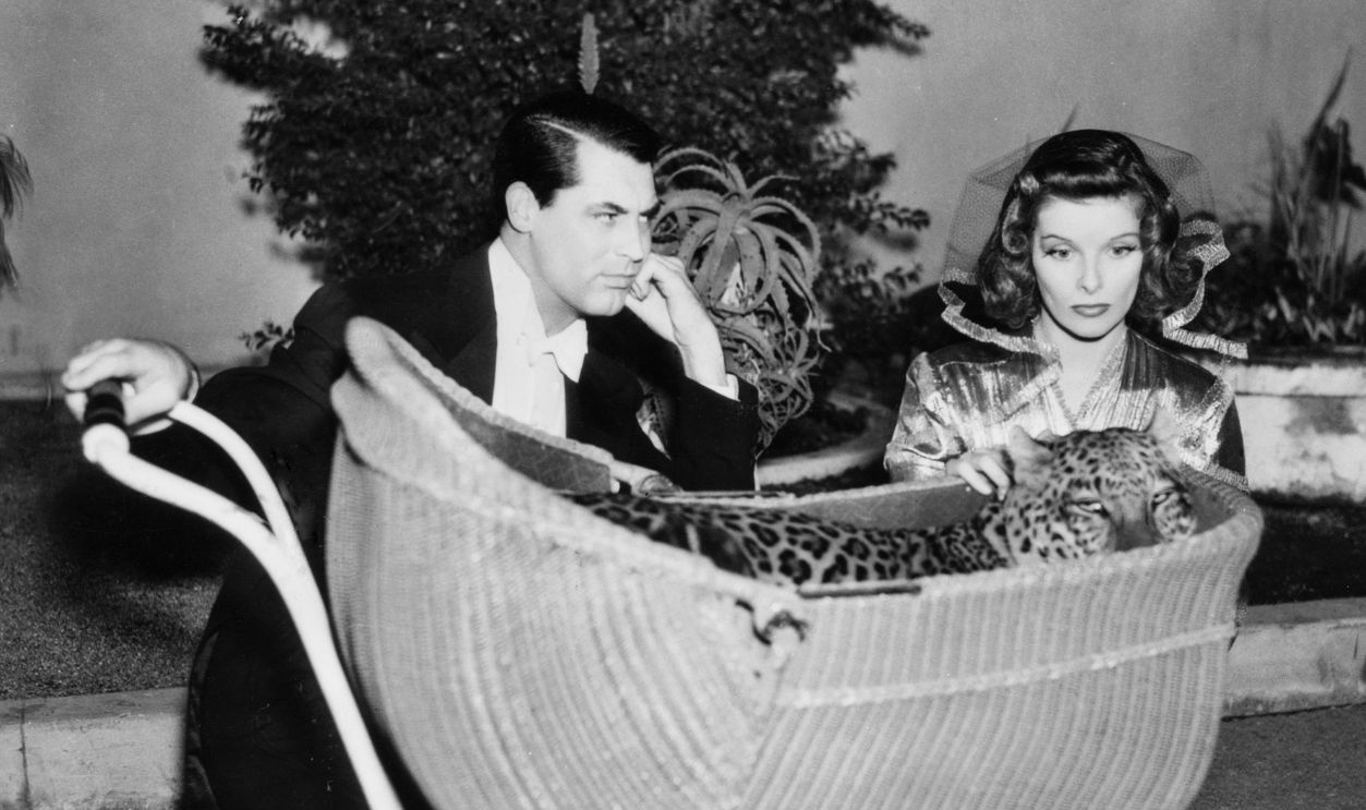 David Huxley and Susan Vance (Cary Grant and Katharine Hepburn), sit in a park with Baby, a leopard, resting in a baby carriage. 