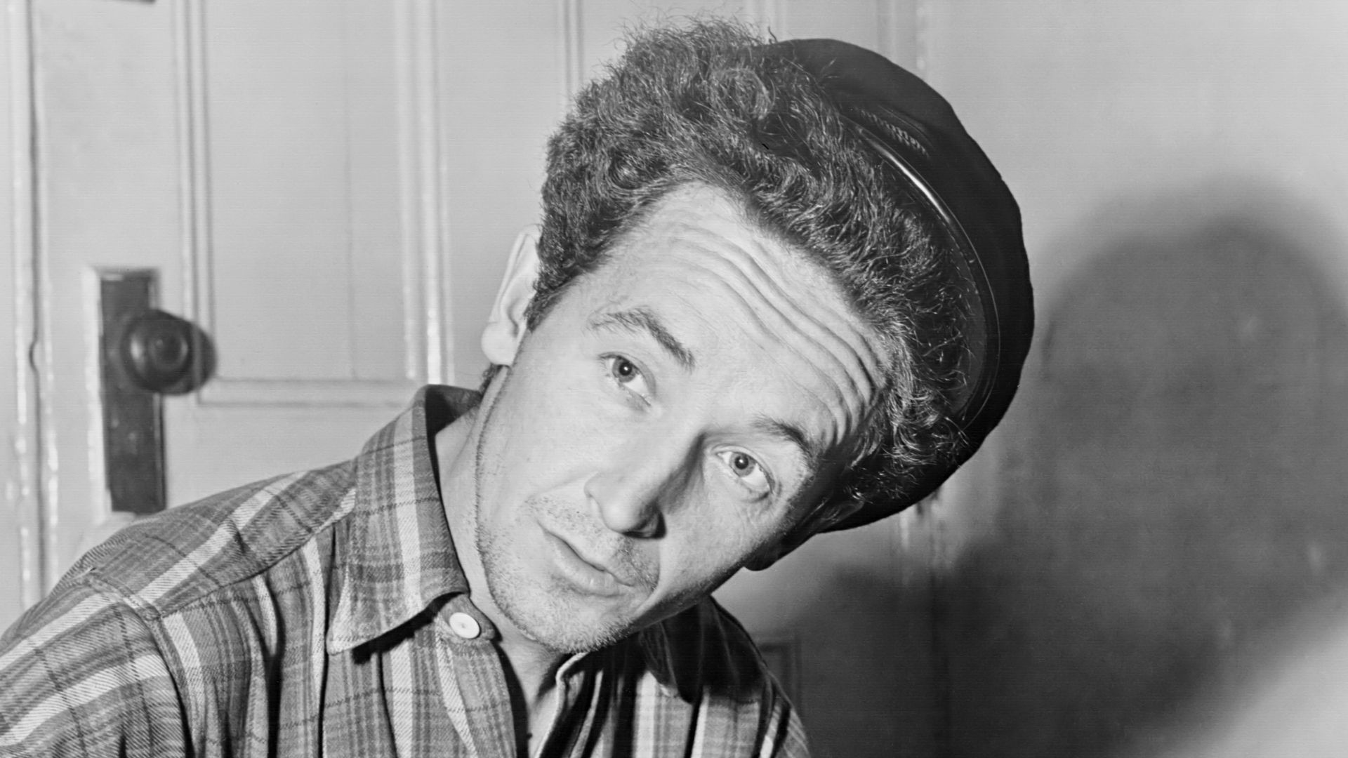 Title: Woody Guthrie, half-length portrait, seated, facing front, playing a guitar that has a sticker attached reading: This Machine Kills Fascists