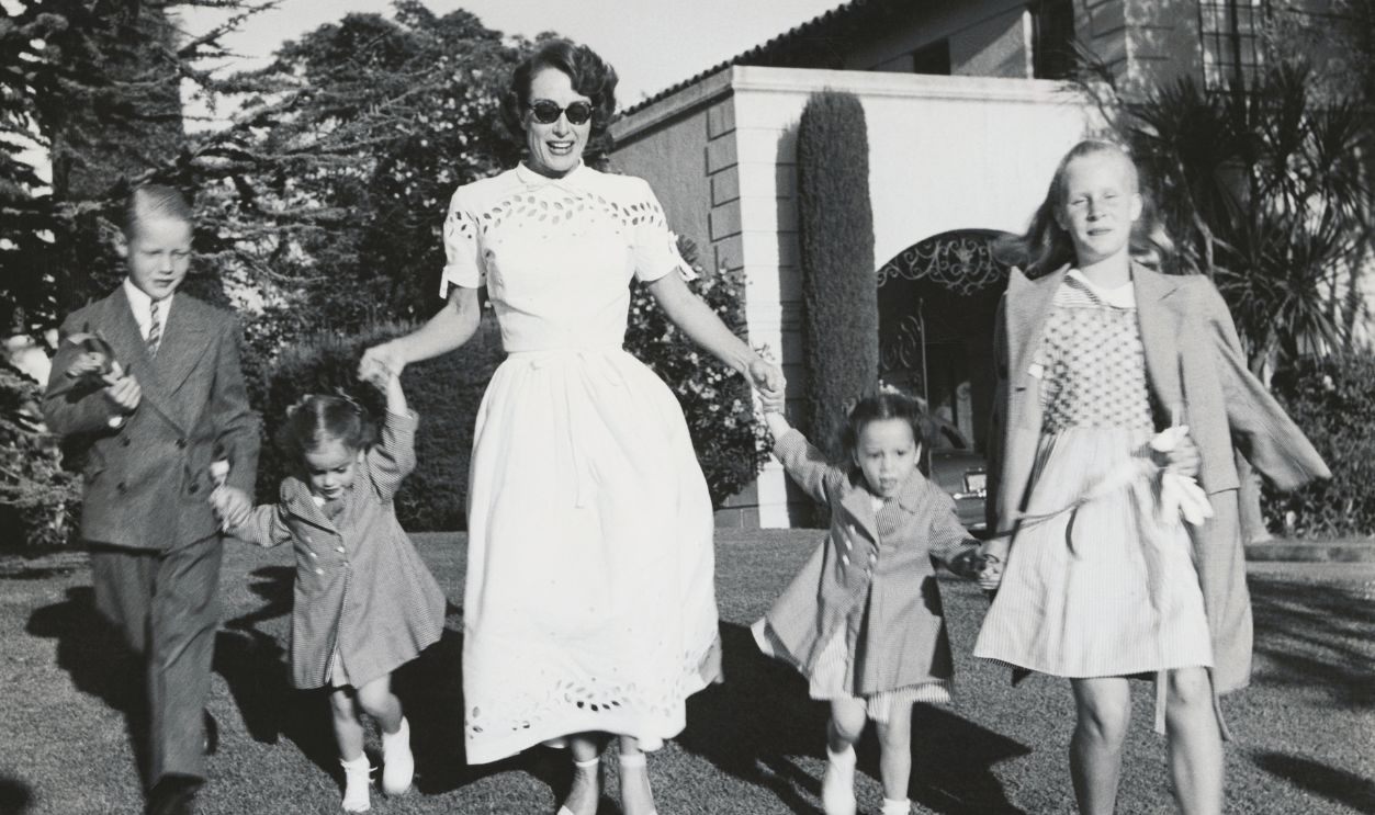 Joan Crawford and four children, Christopher, Cathy, Cynthia, and Christina romp on lawn following party given by Ann Rutherford for daughter Gloria's 5th birthday.