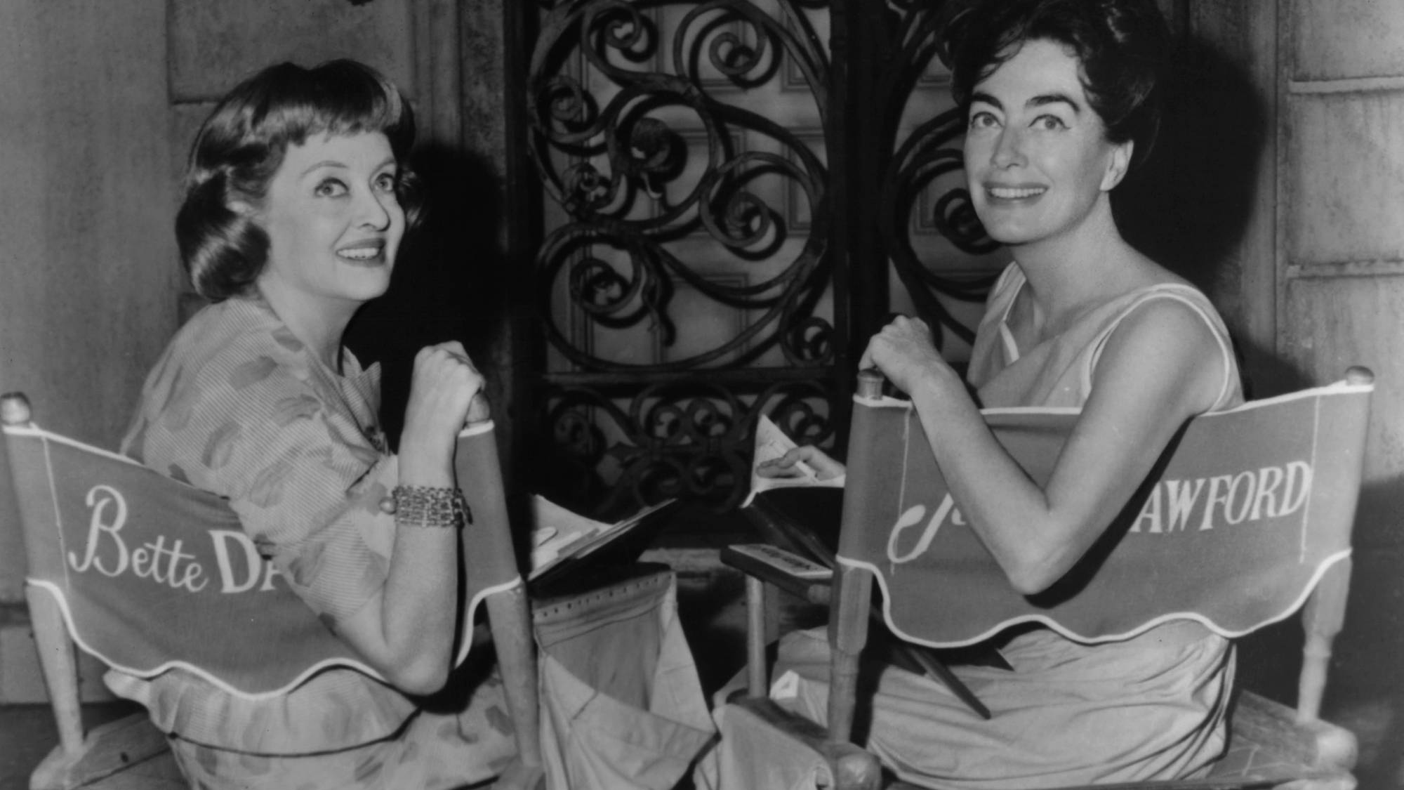 Bette Davis and Joan Crawford  seated on chairs with their names on