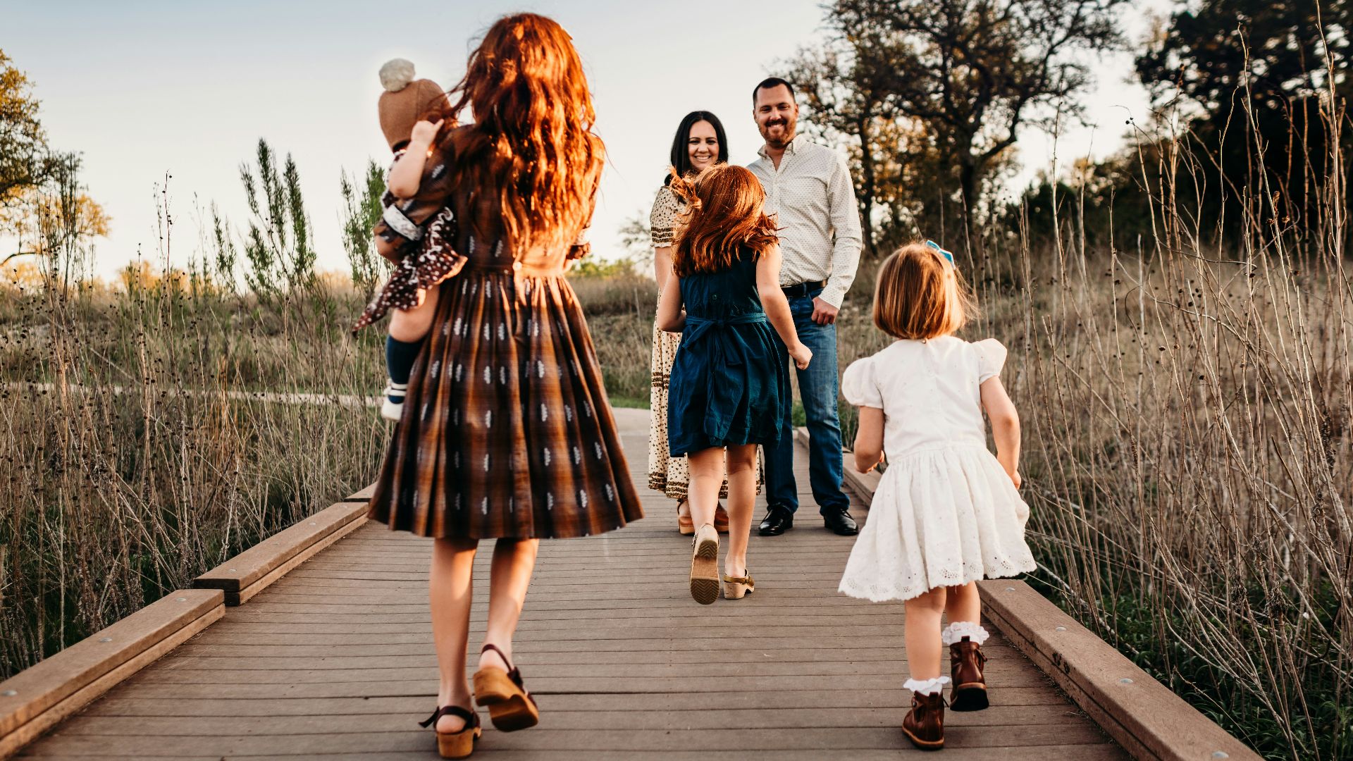A family walking along a wooden boardwalk in a field during golden hour