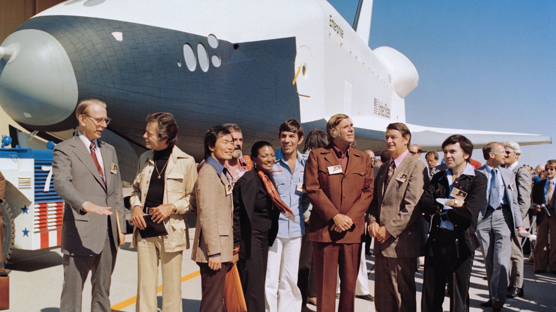 Enterprise, Orbiter Vehicle (OV) 101, rolls out of the Palmdale manufacturing facilities with Star Trek television cast members and Dr. James D. Fletcher present for the ceremony, 09/17/76. Left to right are Fletcher, DeForest Kelley, George Taki, Nichell