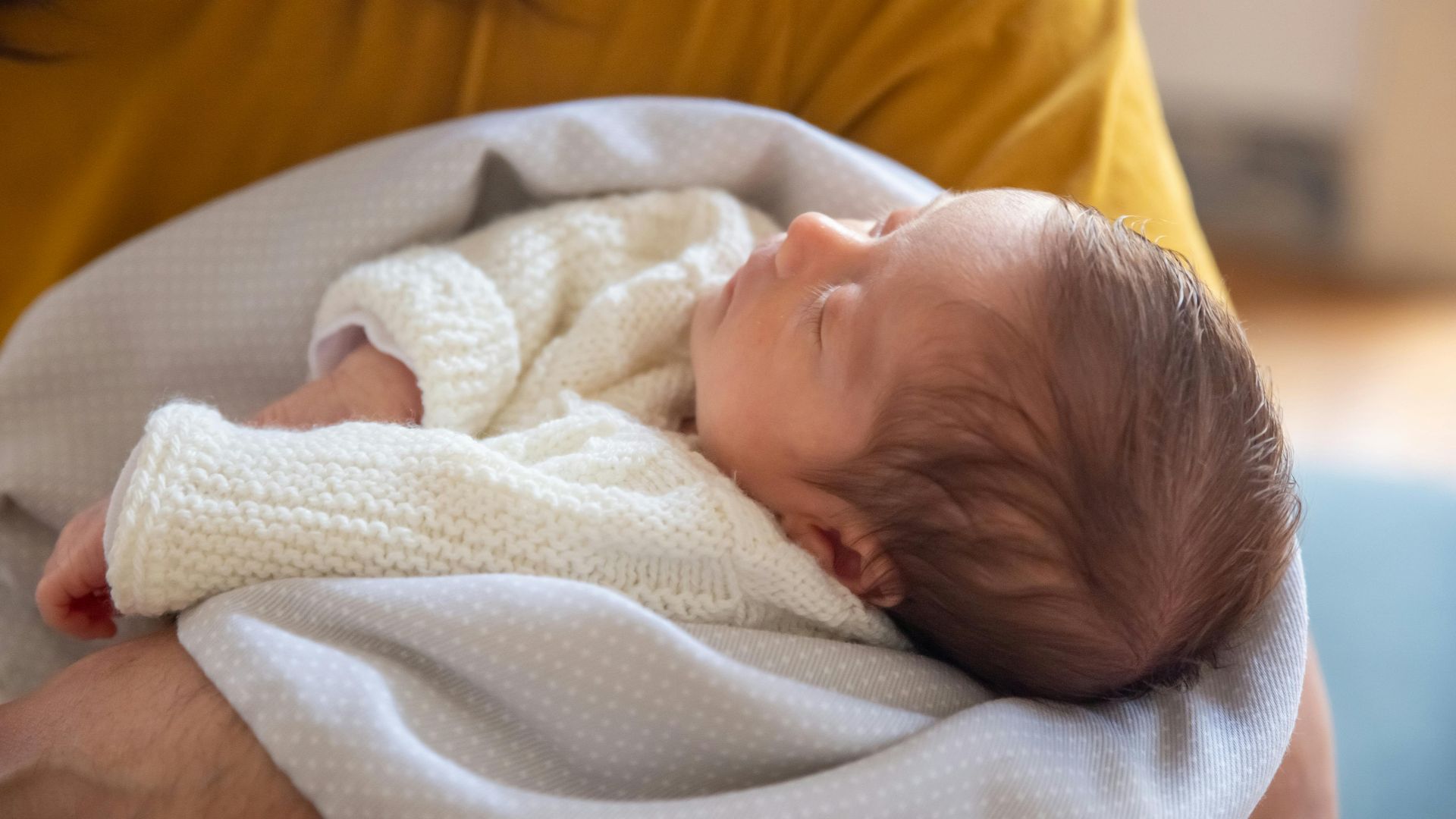 Close-up of a peaceful newborn baby sleeping in a parent's arms indoors.