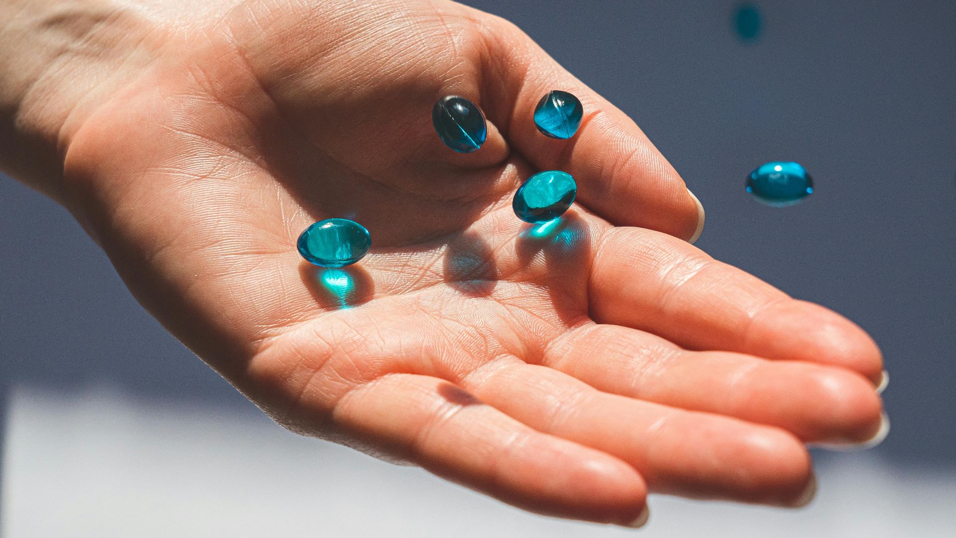 A close-up photo of a hand holding blue capsules, against a neutral background.