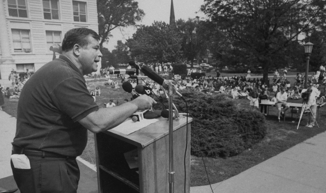Ex-actor/self-proclaimed pres. cand. Tom Laughlin speaking from podium as he addresses students at a rally protesting education budget cuts at the Univ. of Iowa during his campaign tour of the state. 
