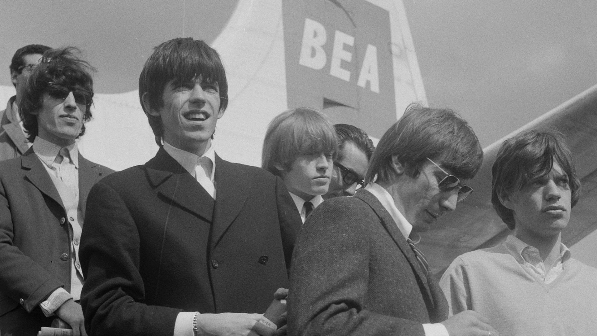 The Rolling Stones getting off an airplane at Amsterdam Airport Schiphol on August 8, 1964. Mick and Keith are holding a bottle of Bols jenever.