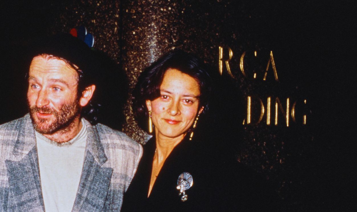 Gettyimages - 2233371588, Robin Williams & Marsha Garces American actor and comedian Robin Williams, wearing a plaid suit jacket, with partner Marsha Garces, wearing a black coat adorned with a brooch, outside the RCA Building in in New York City, circa 1988. 