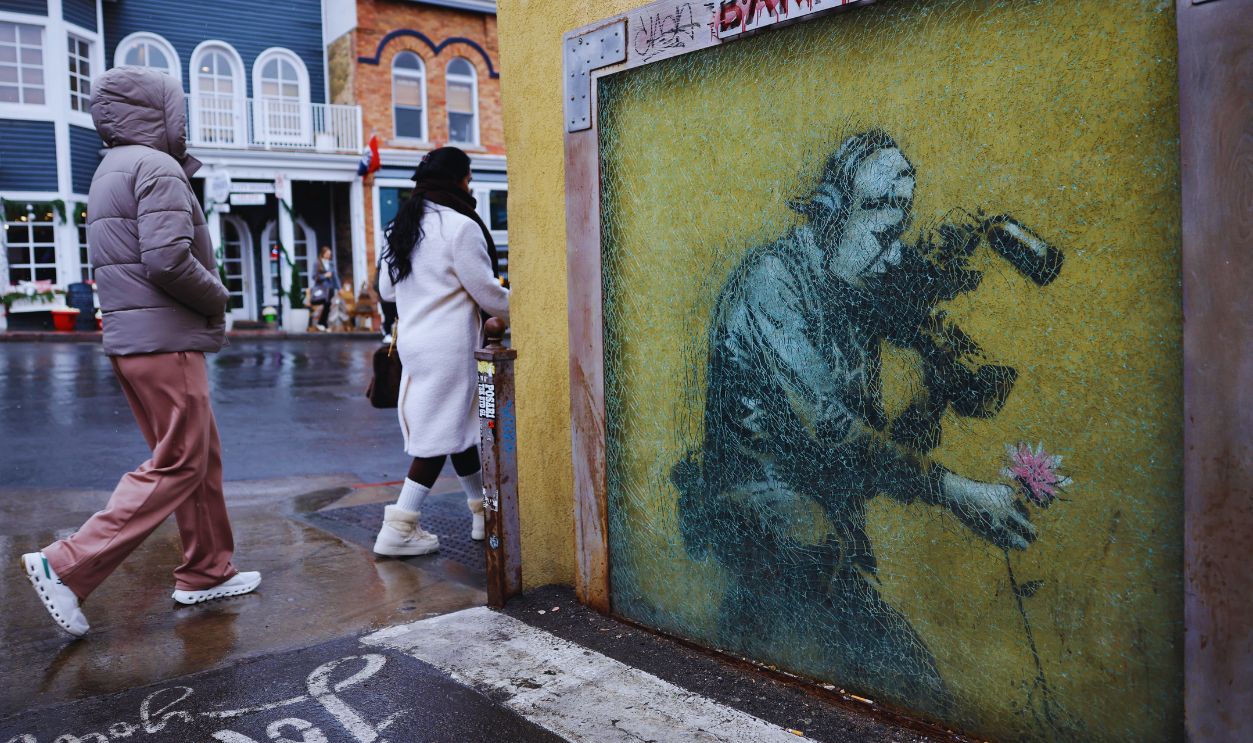 Gettyimages - 2260772596, People walk past a Banksy piece as light snow falls as a significant weather pattern shift begins to deliver snow to Utah's mountains in the region on February 9, 2026 in Park City, Utah. 