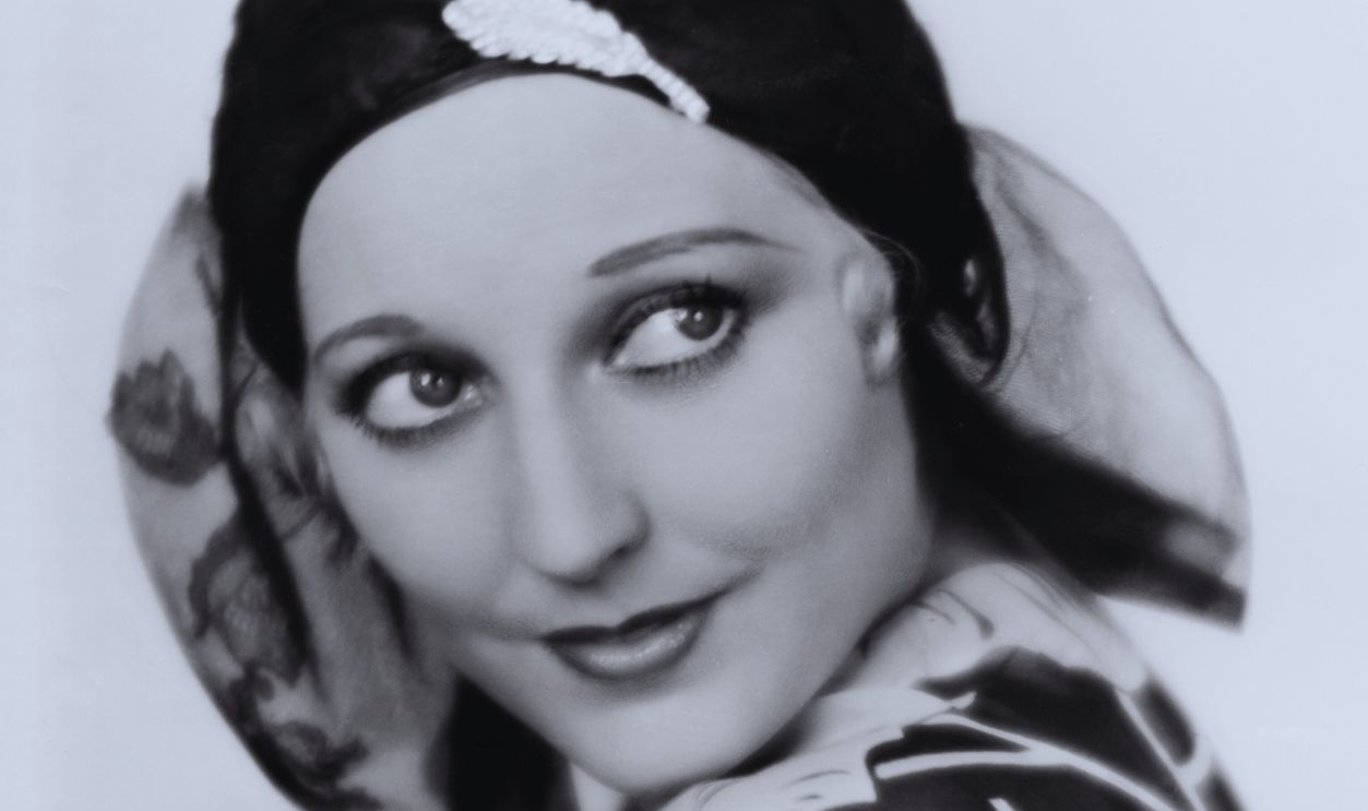 Actress Thelma Todd in Blue Chiffon Actress Thelma Todd wearing a navy blue chiffon gown with a floral design in white and a maline off-the-face hat of navy blue, with a rhinestone pin. 