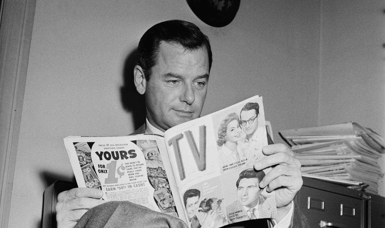 Gig Young Goes Shopping American actor Gig Young (1913 - 1978) reading the November 1955 copy of 'TV' magazine, USA, 1955.