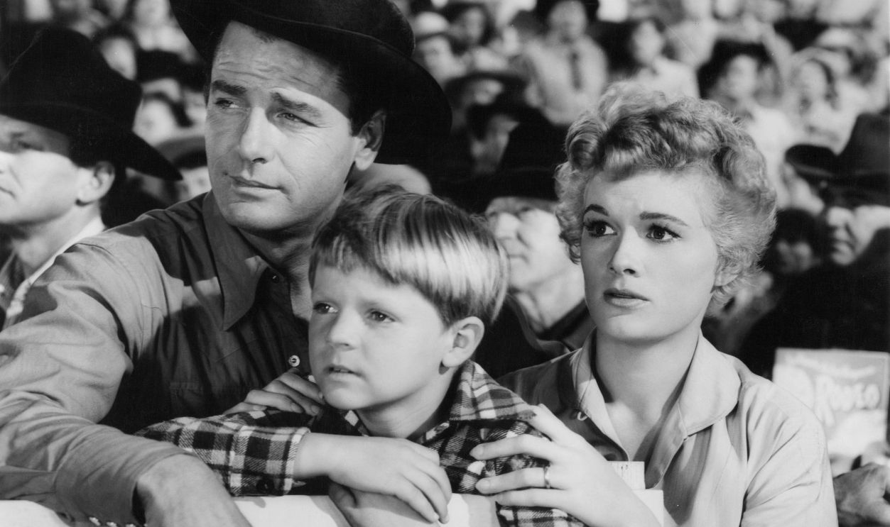 Gig Young, Lee Aaker, and Jean Hagen in the crowd watching the rodeo in a scene from the film 'Arena', 1953.