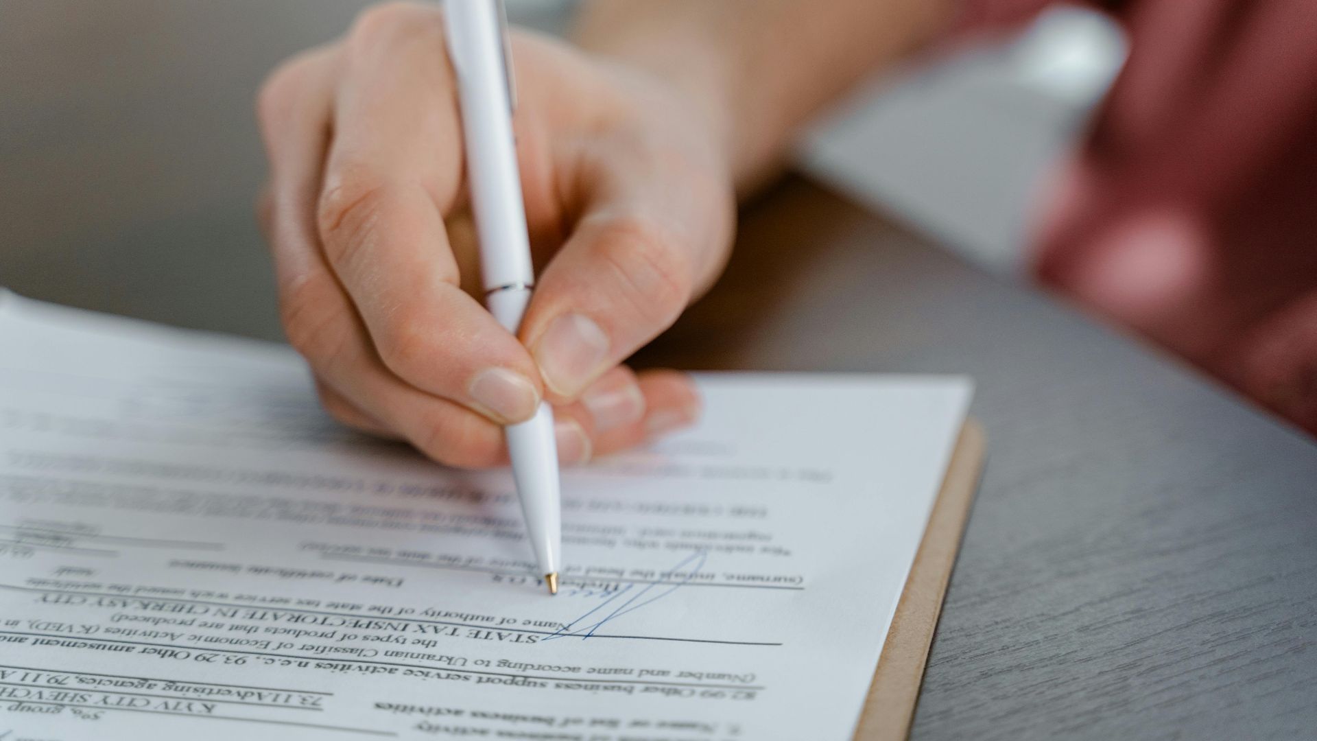 Detailed view of a hand writing a signature on an official document with a ballpoint pen.