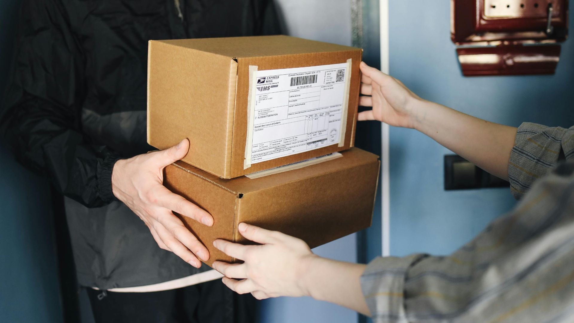 Close-up of hands exchanging cardboard boxes indoors, symbolizing delivery service.