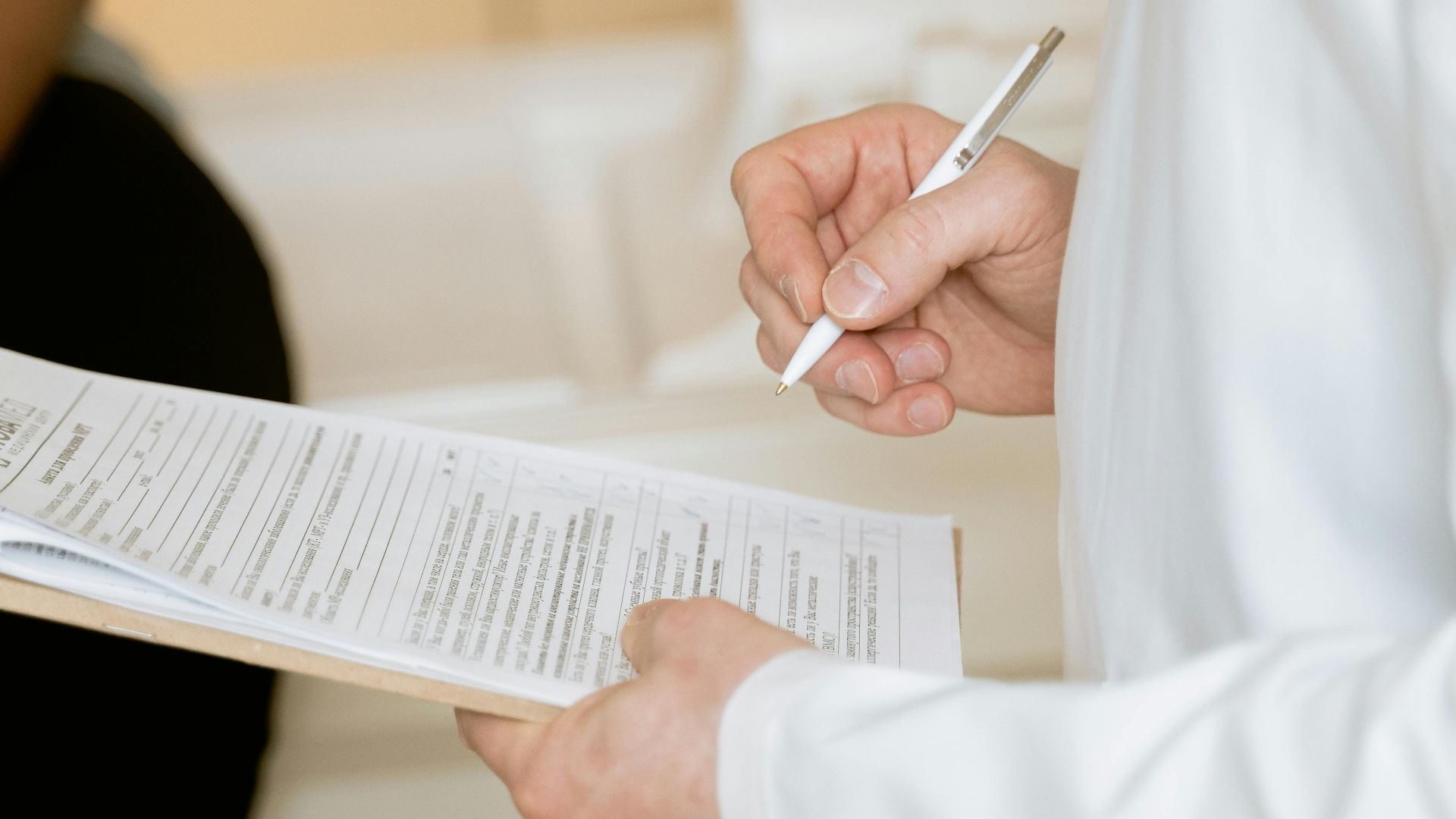 A medical professional in a white coat examines a clipboard with patient documents.