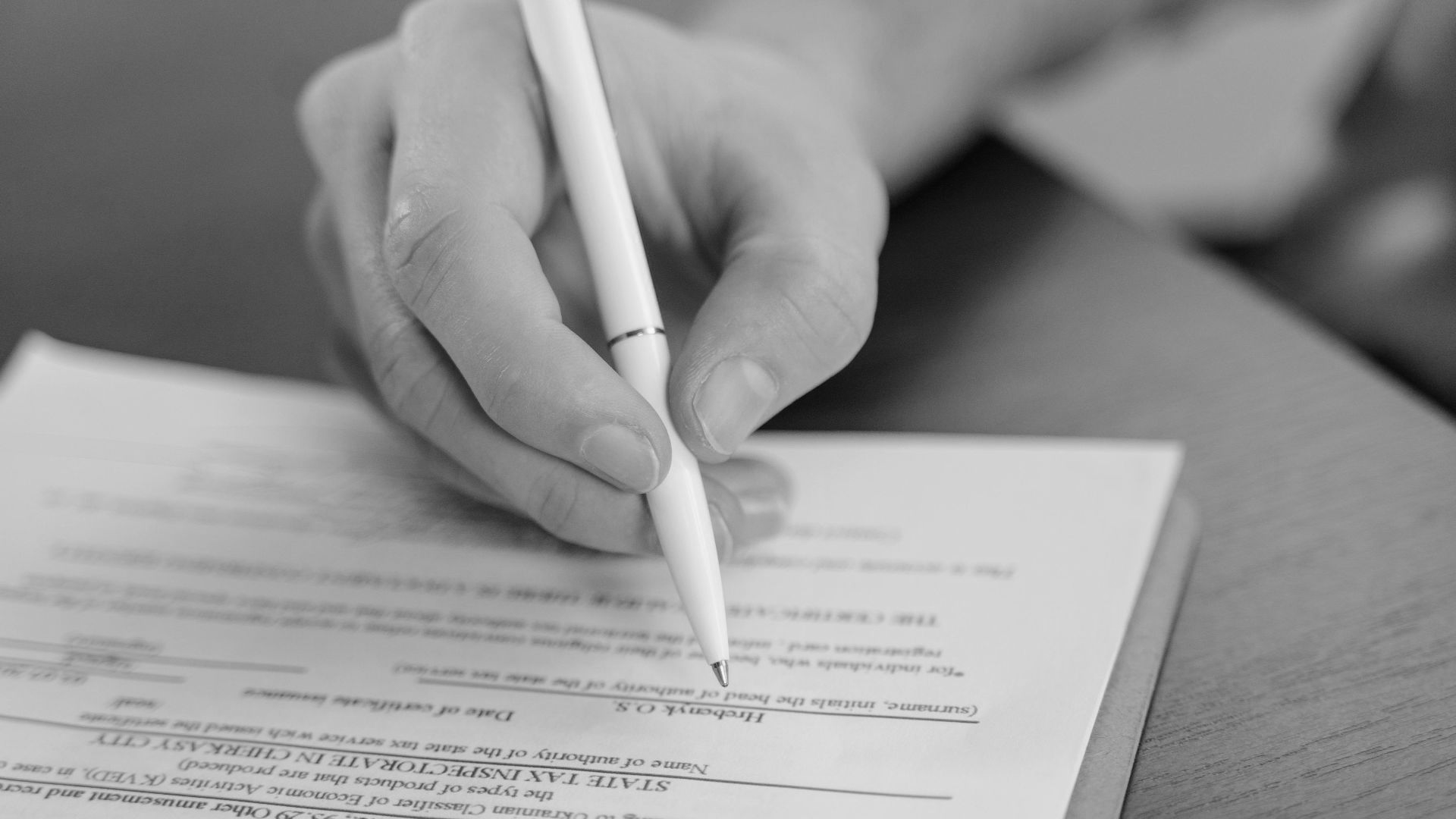 A hand holding a pen signing a document, close-up shot with focus on the paper.