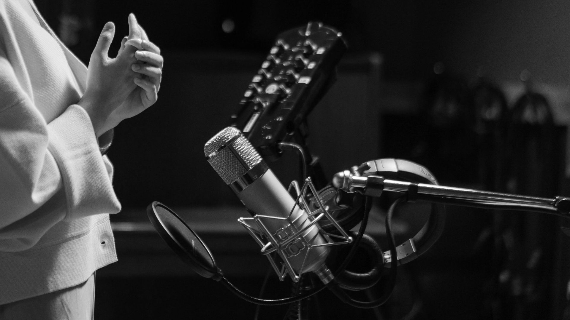 Side view of a woman singing into a condenser microphone in a professional recording studio.