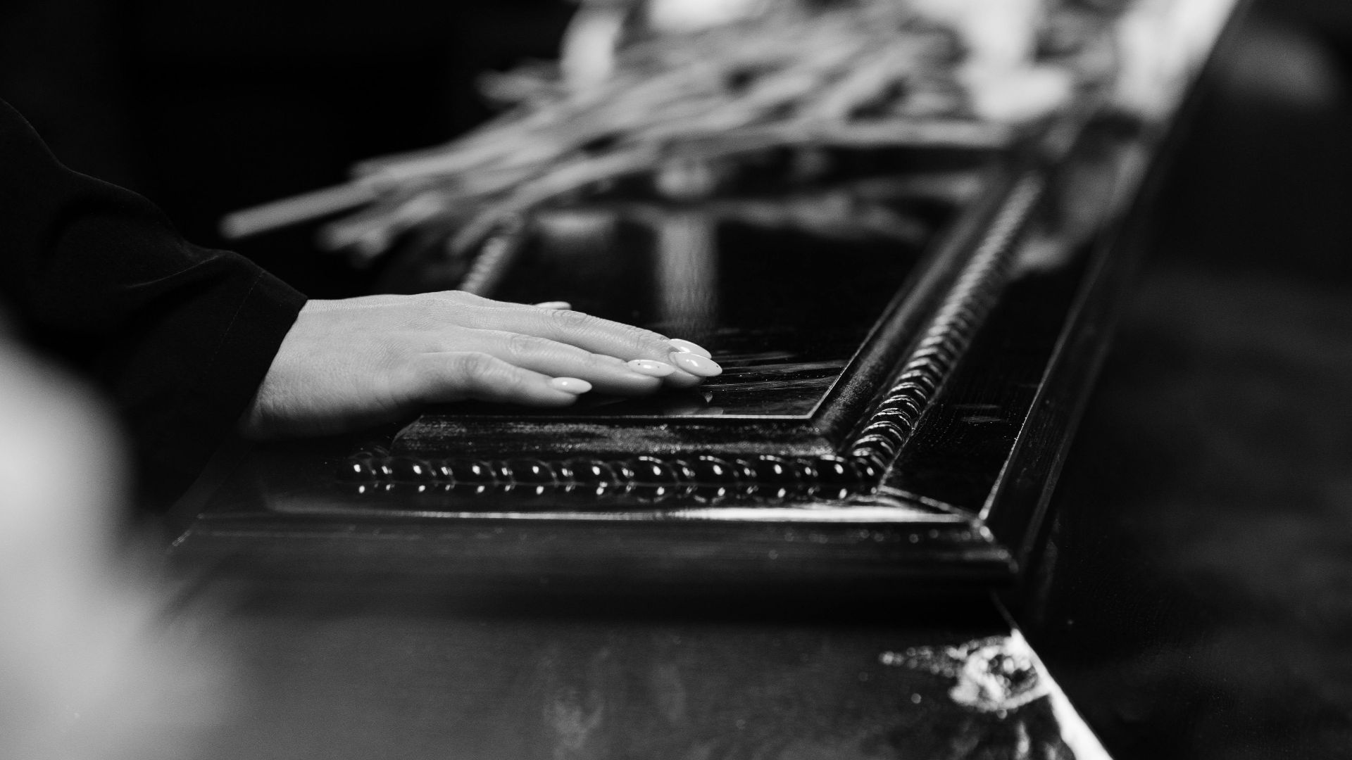 A woman's hand rests on a casket, conveying a poignant moment of farewell during a solemn funeral.