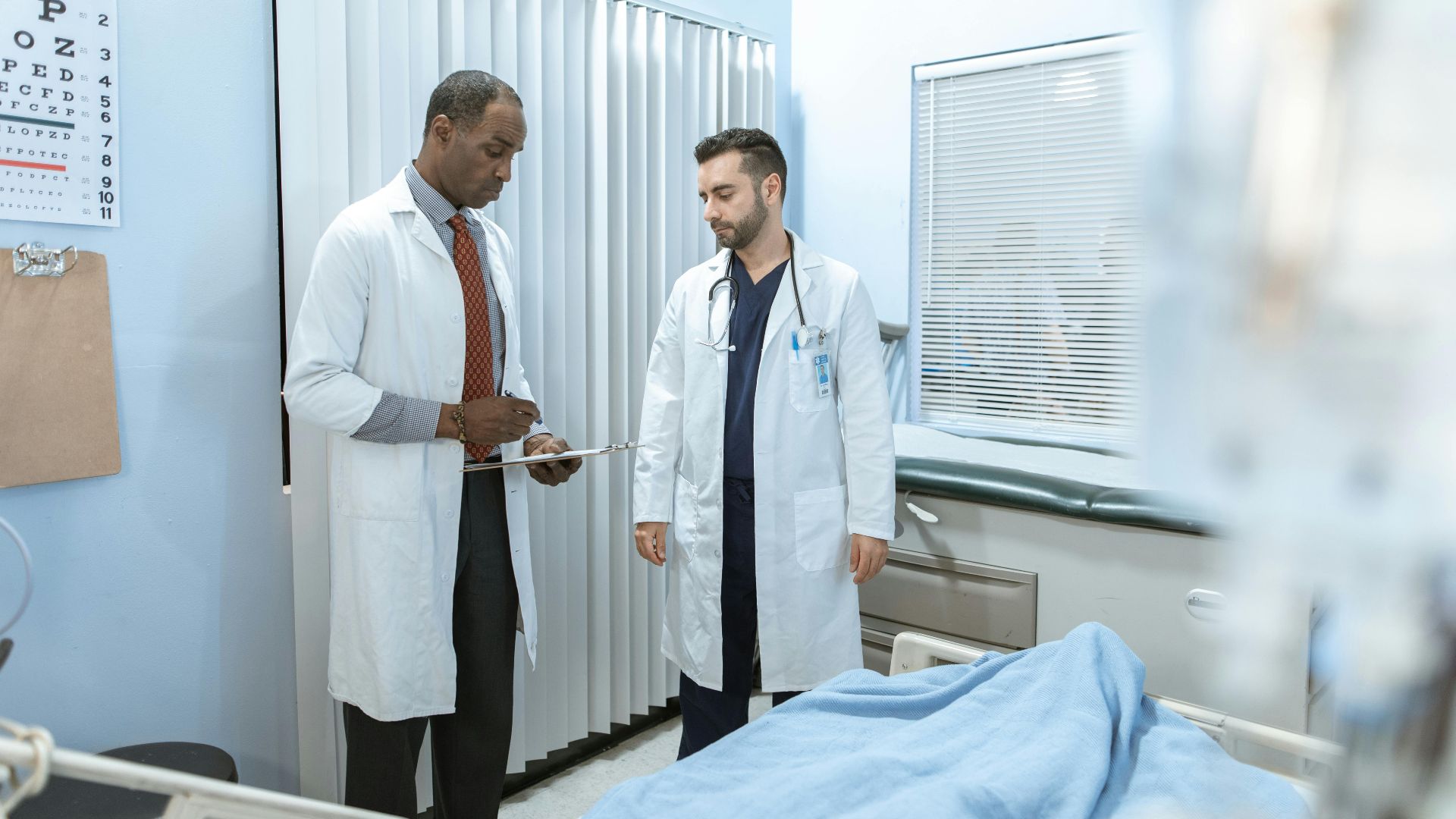 Two doctors review a patient's chart in a hospital room, focusing on healthcare cooperation and medical care.