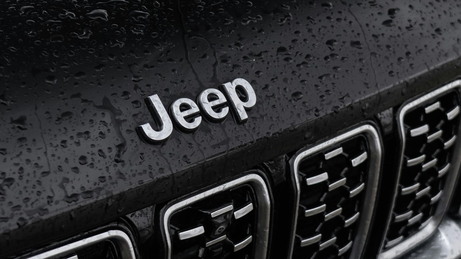 A detailed view of a black Jeep SUV parked outdoors, showcasing rain droplets on the hood.