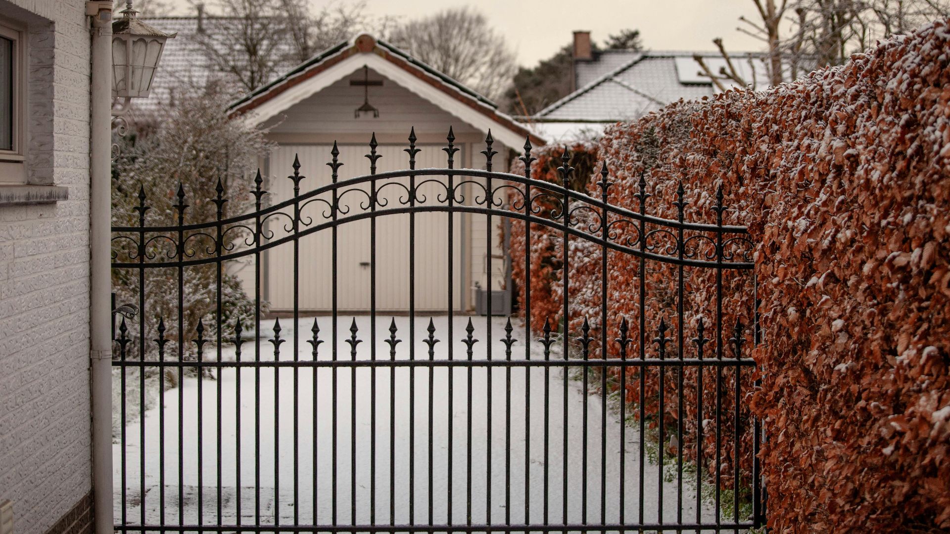 A serene snowy courtyard featuring a decorative iron gate and surrounding hedges in winter.